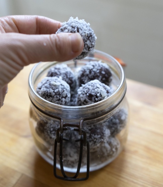 Je ziet een hand die bliss balls vast heeft.