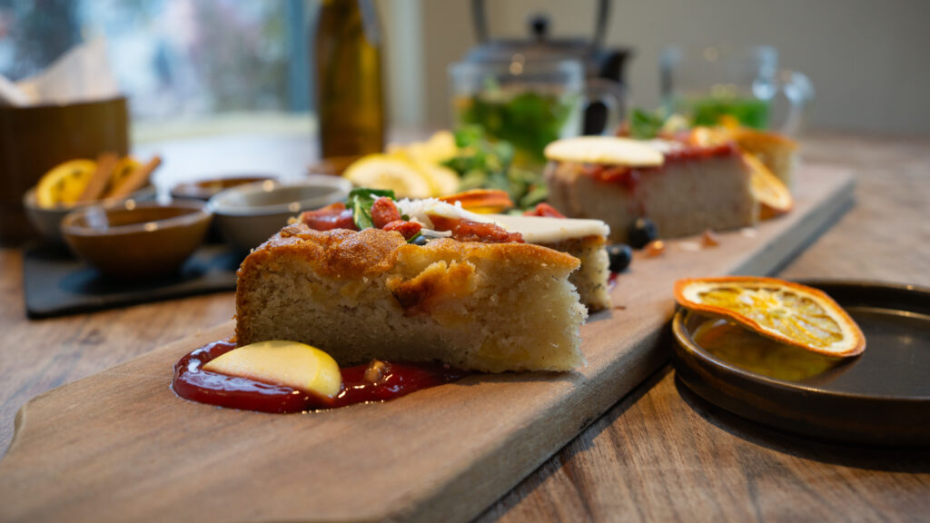 Stukjes vegan, glutenvrije taart geserveerd op een houten plank als onderdeel van een high tea-arrangement. Vergezeld van een theepot.